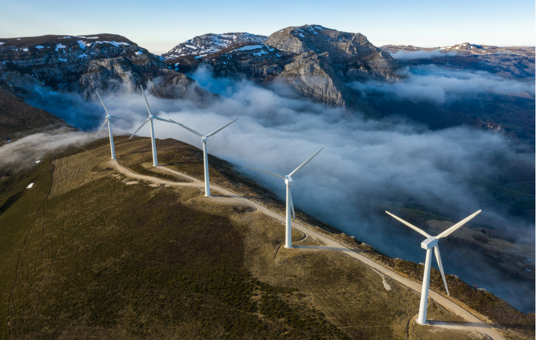 Mountain range peeking through fog in background, wind turbines lining mountaintop in foreground