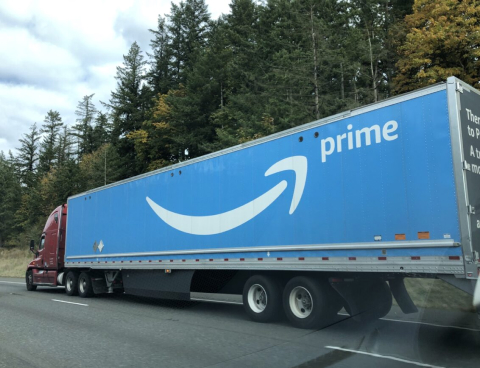 Amazon Prime fleet truck driving on a highway lined with trees